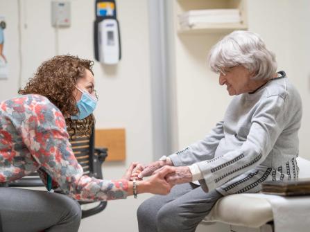 A seated provider holding hands with a seated geriatric patient in an exam room