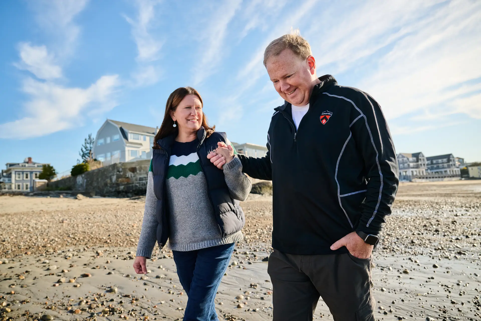 Lisa and Jeff Clark walking on the beach, blue sky behind them