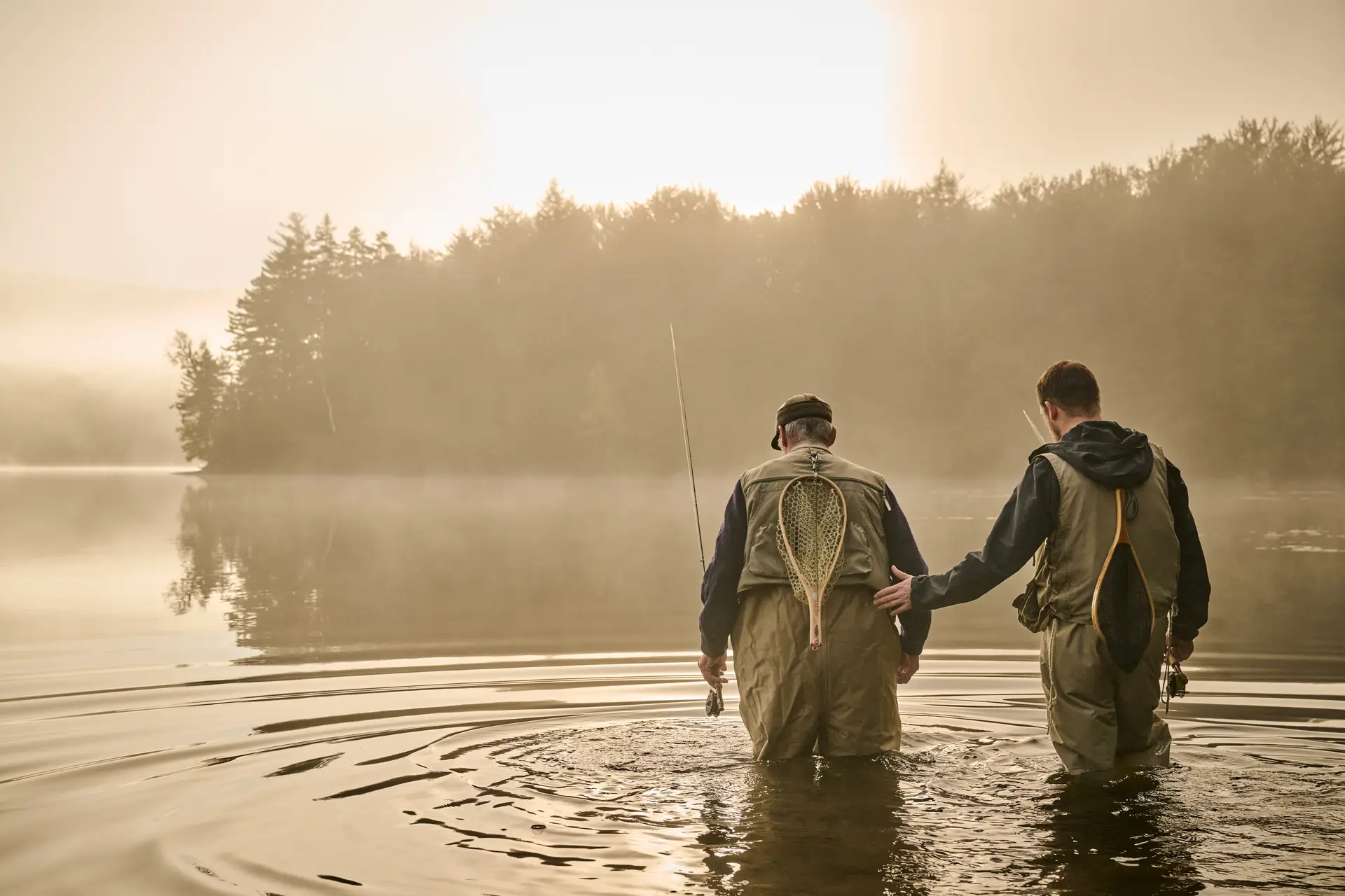 Two fishermen wade in shallow waters of a lake at sunrise