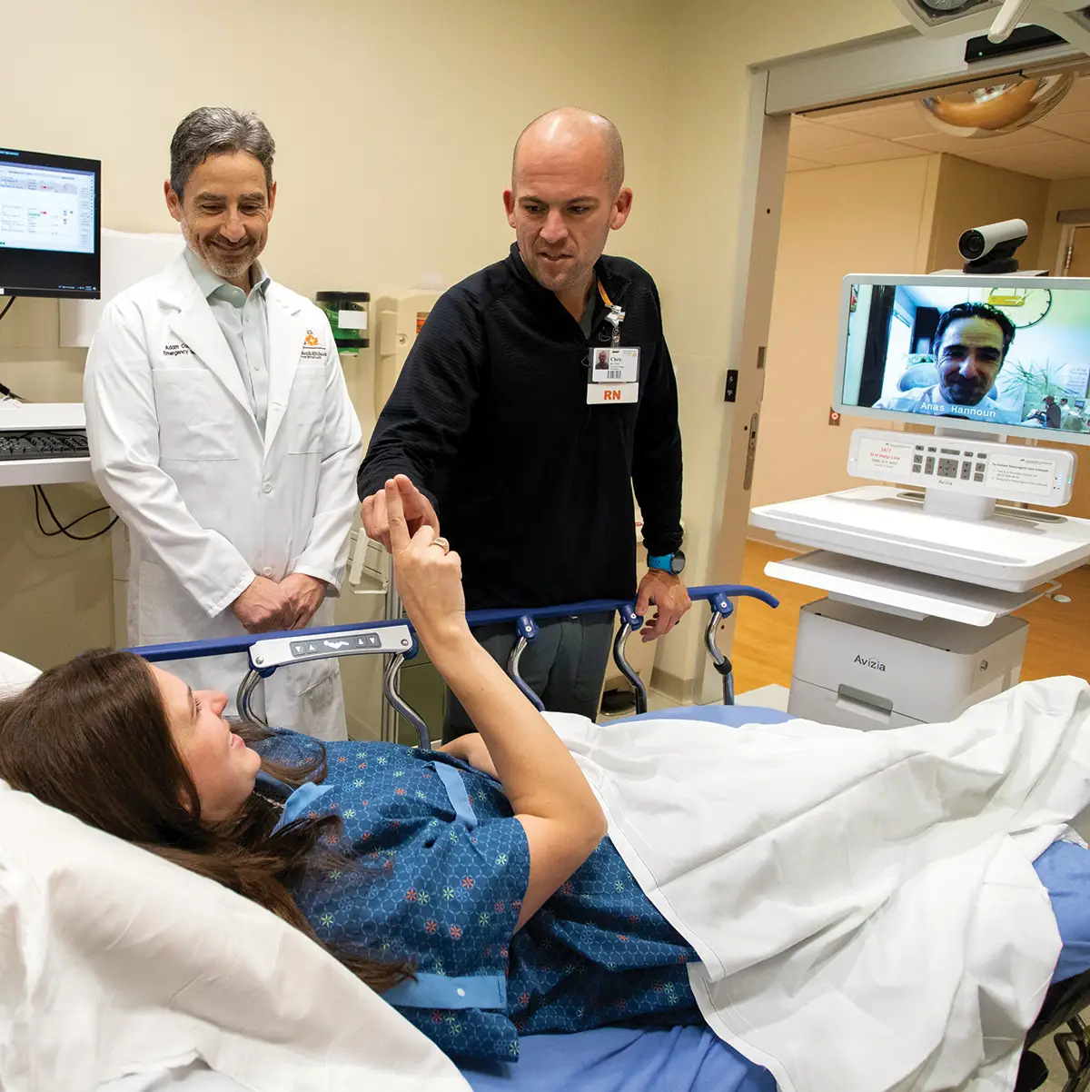 two male healthcare providers speak to a patient in a hospital bed