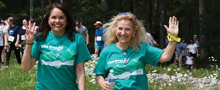 smiling people walking in a wooded area and waving at the camera
