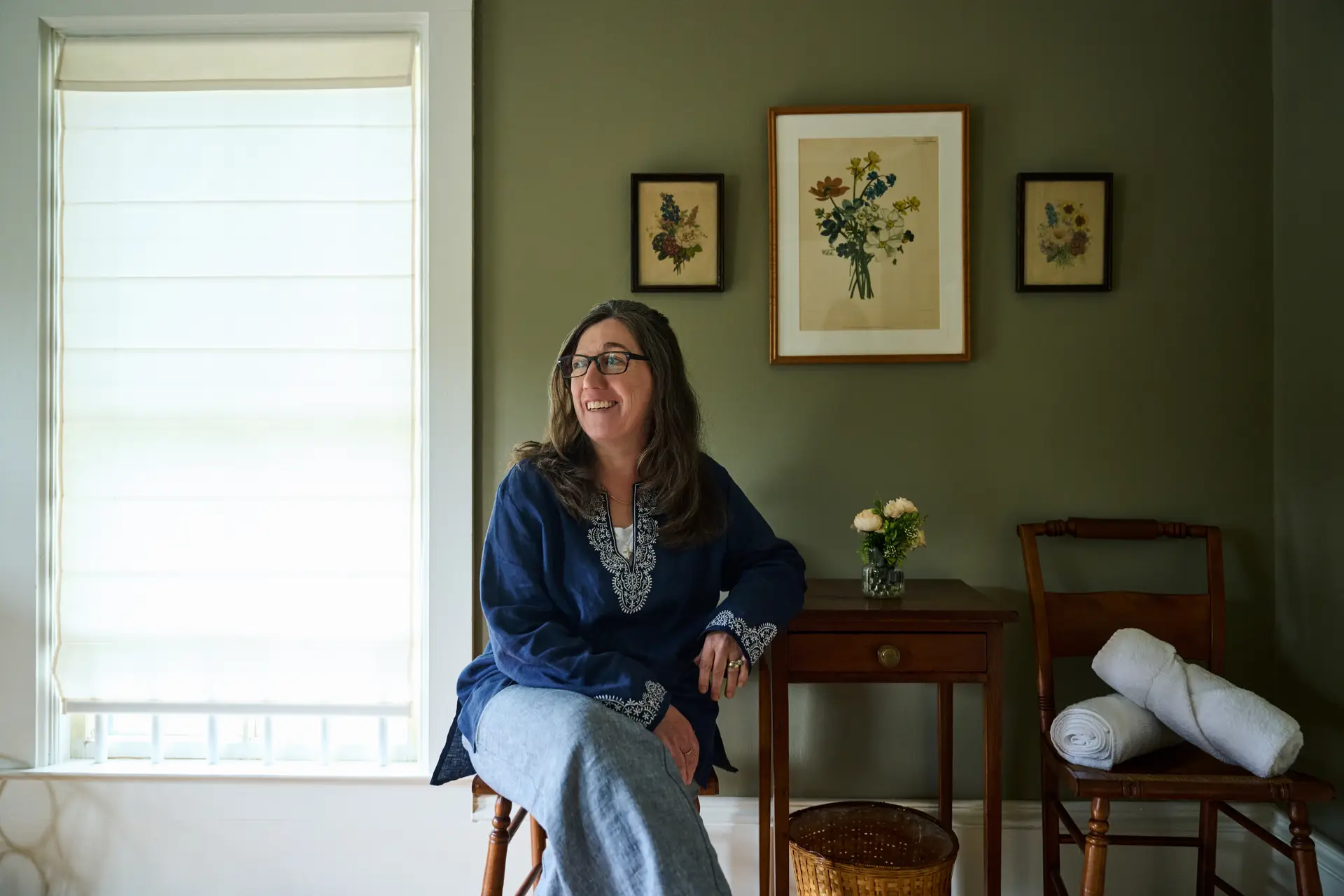 Woman sits in a room, smiling and leaning on a small table