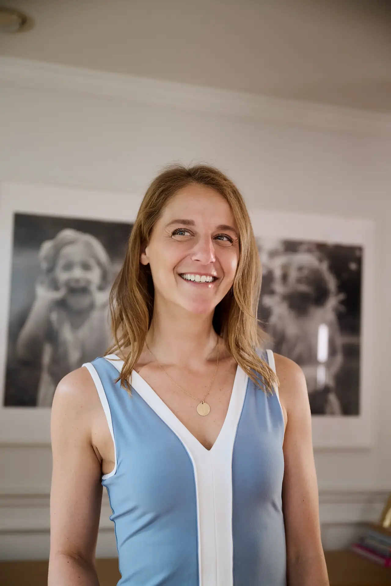 Smiling woman stands indoors in front of large black and white photos of a childe