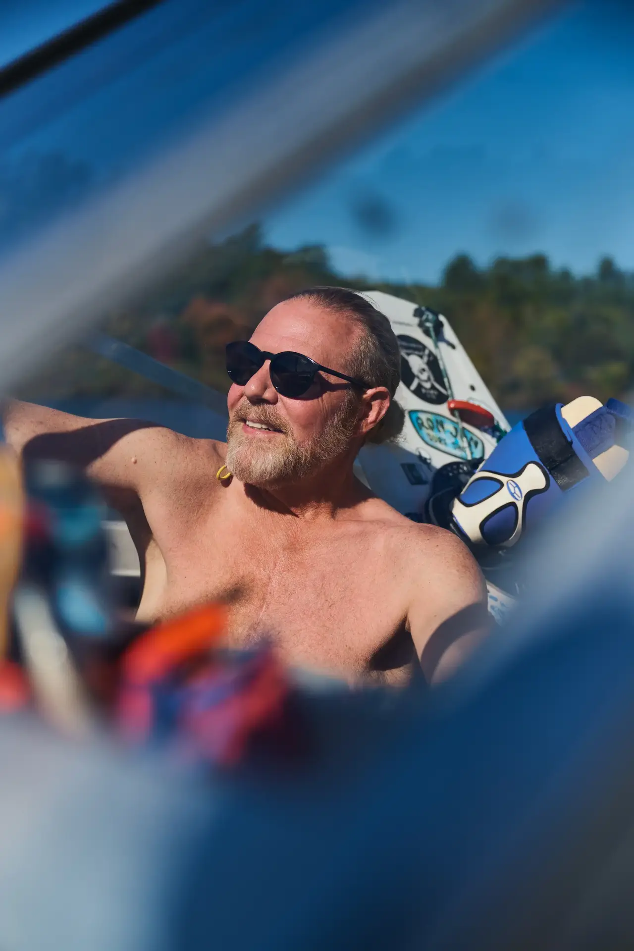A shirtless man with sunglasses on sitting in the sun