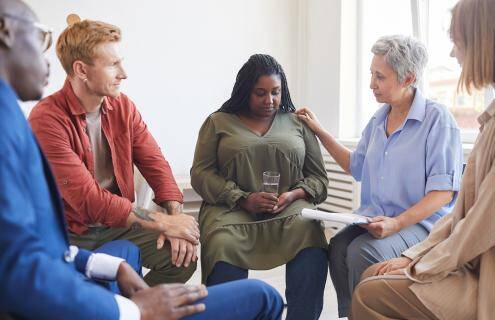 A diverse group of people sitting in a circle, one woman consoles another.