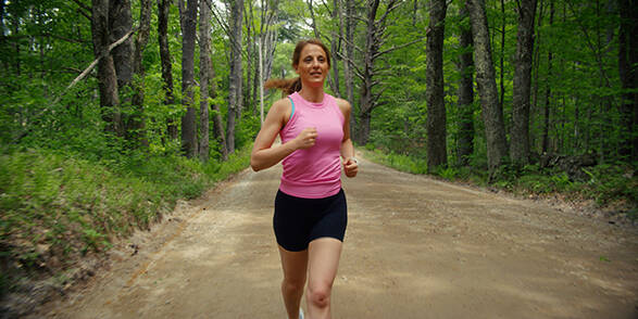 A woman jogging on a dirt road in the forest