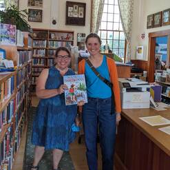 Two women hold up a picture book in the children's section of a library