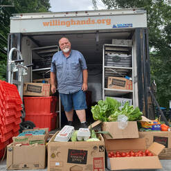 A man stands in the back of a Willing Hands truck with boxes of fresh produce in front of him