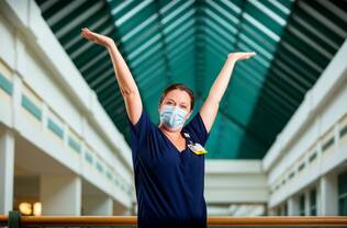 A nurse inside Dartmouth Hitchcock Medical Center raising her arms in welcome