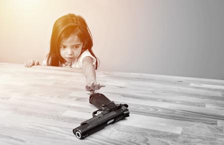 A child reaching across a table to a handgun