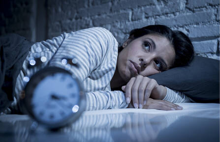 Woman laying in bed next to a clock.