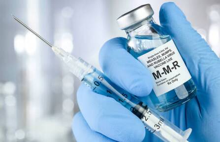 Gloved hand holds MMR vaccine vial and syringe