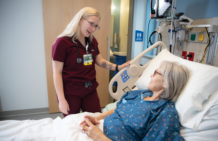 Nurse Alexis E. Morin, RN, pictured standing at the bedside of a female patient in a hospital room.
