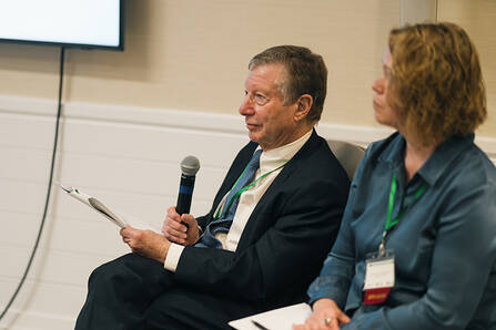 Two seated speakers in a conference room, one holding a microphone