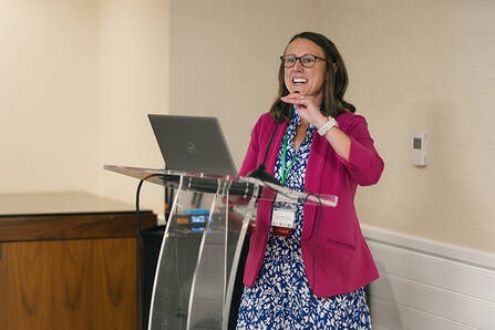 A woman standing at a lectern with a laptop in a conference room