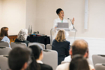 A speaker standing at a lectern with a laptop in front of an audience in a conference room