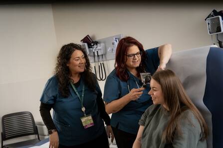 Two nurses look in the ear of a patient.