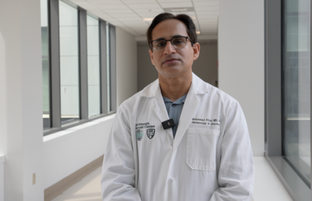 Dr. Afzal stands in a hallway with many windows.