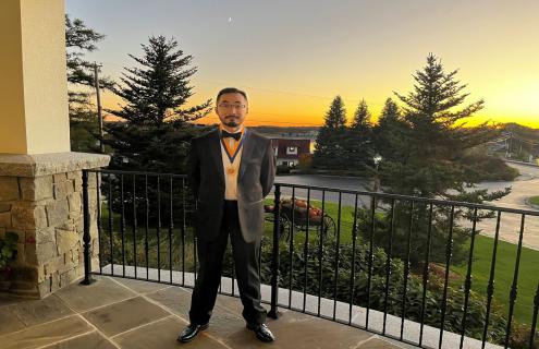 Eric Loo, MD, wearing a suit and a medal, standing on a balcony with a sunset behind him, crescent moon in the sky