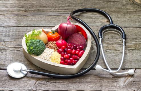 Fresh fruits and vegetables in a heart-shaped wooden box next to a stethoscope