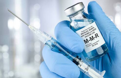 Gloved hand holds MMR vaccine vial and syringe