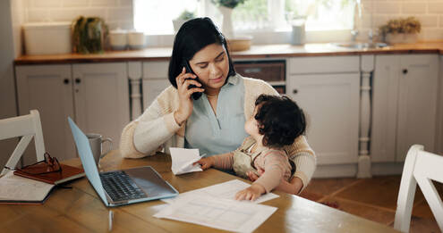 Woman multitasking at kitchen table with child.