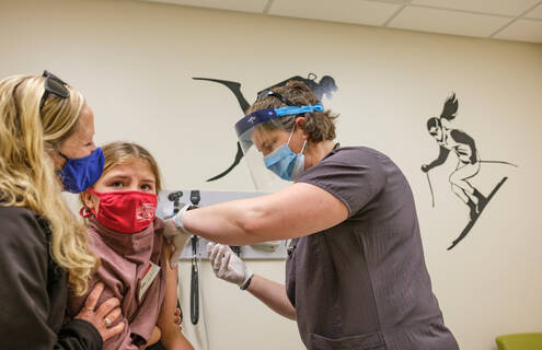 Photo of child being vaccinated by female provider to her right with her mother to her left