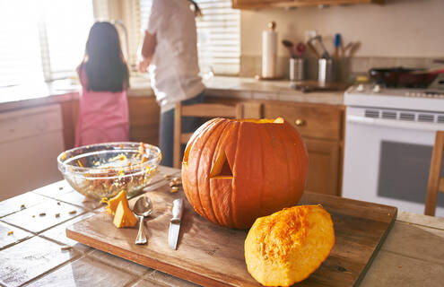 Picture of carved pumpkin in kitchen with two people at sink