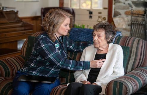 Female nurse uses stethoscope to listen to listen to heartbeat of elderly female patient in her home