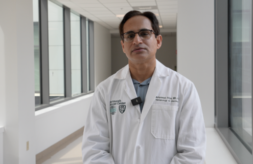 Dr. Afzal stands in a hallway with many windows.