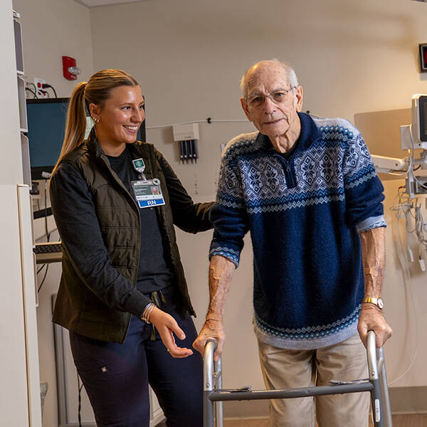 A provider helps an older patient using a walker