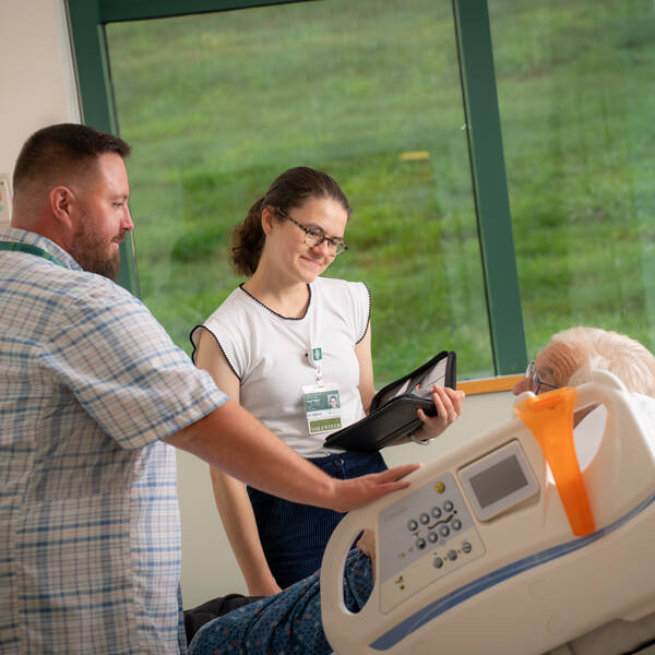 Two healthcare providers speak to a patient in a hospital bed