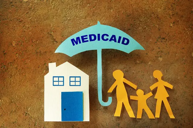 cut paper illustration depicting a house and a family under an umbrella bearing the word Medicaid