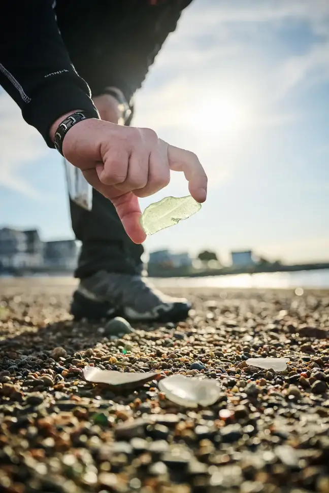 The hand of Jeff Clark reaching for a piece of seaglass on the beach