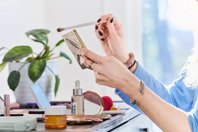 A woman's hands hold a makeup brush and small vanity