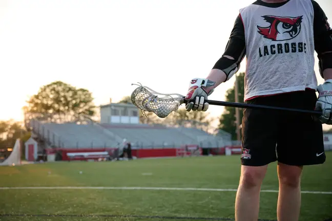 A man, shown from neck down wearing Lacrosse gear, stands on a field