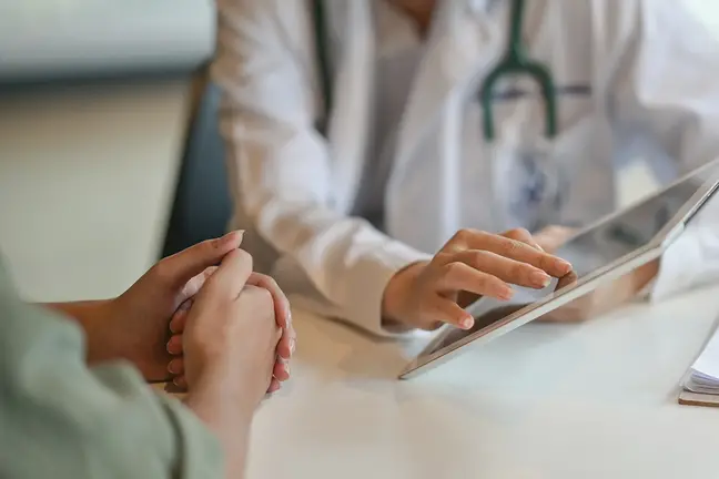 Clasped hands of a woman next to hands of a a female healthcare provider holding a tablet