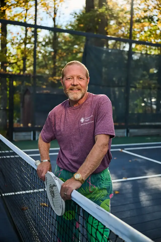 Man holding a tennis racket stands at the net of a tennis court