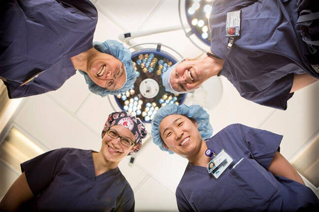 Four smiling nurses look down on a patient in bed