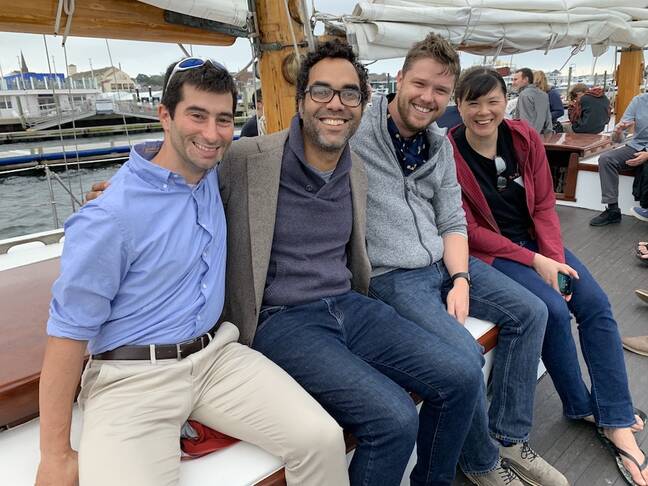 Three men and a woman smiling and enjoying a day on a sailboat